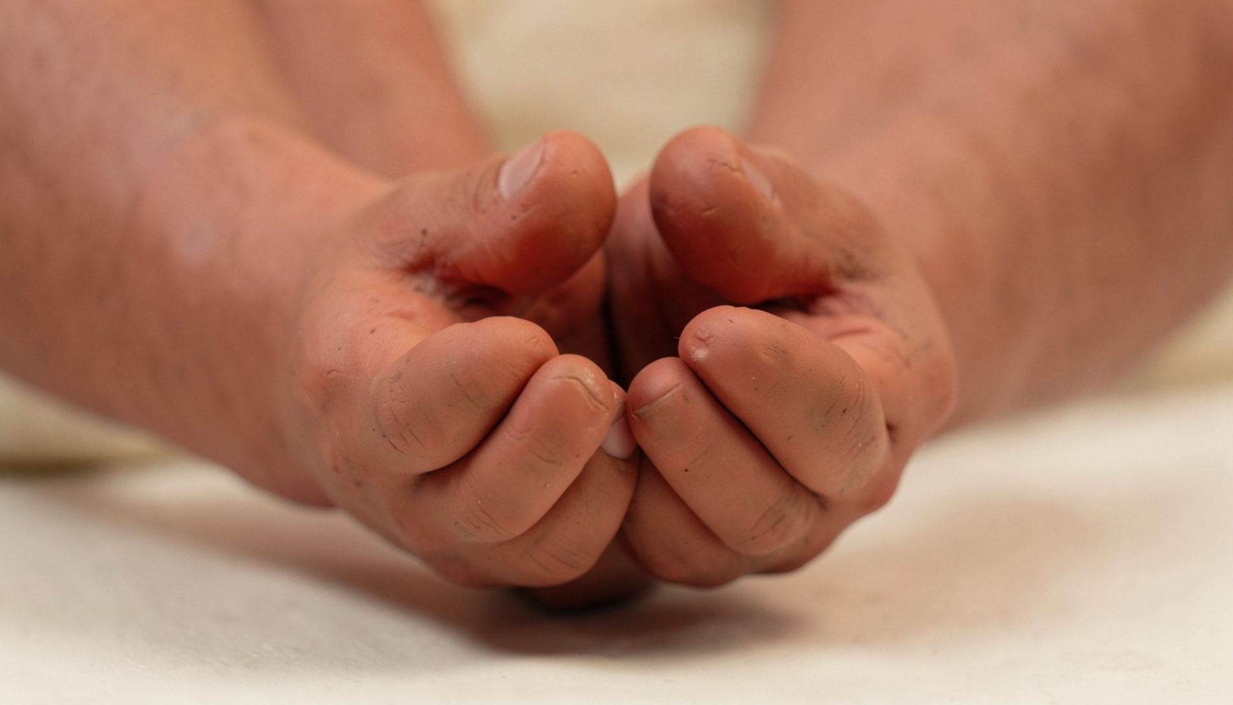 A soft clay-model scene of hands cupped together in a gentle, supportive gesture, rendered in warm earthy browns, muted terracotta, and cream tones against a softly lit background.
